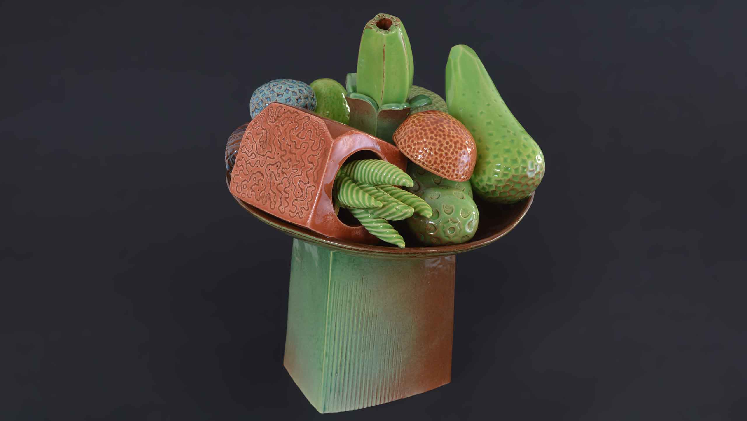 Photograph of 'Abundance' - still life on stand by contemporary ceramic artist Simon Fell: A ceramic still life on a bowl on a tall stand sits a set of unlikely fruits. Something like a banana emerges vertically from a green flower, a box of pointed succulents emerge from a circular opening, a green pear becomes crystalline at one endand a blue dimpled heart sits next to a double ended curvaceous avocado.