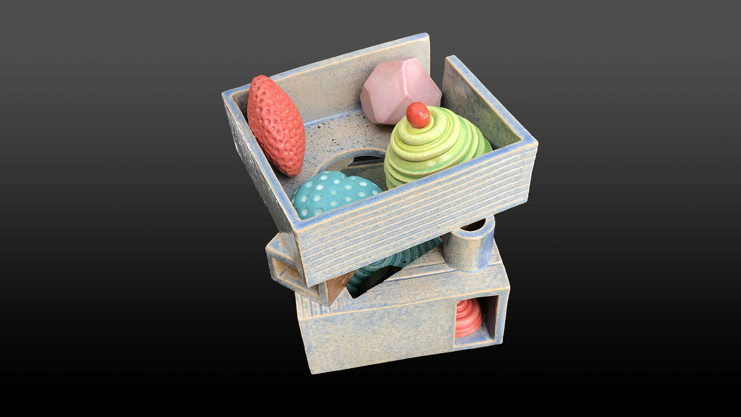 BauWauHaus - a ceramic still-life. Brightly glazed candy-like forms sit in an articulated 'open-plan' grey box on two layers supported on small geometric forms. The two layers are pierced by small rectangular and circular openings