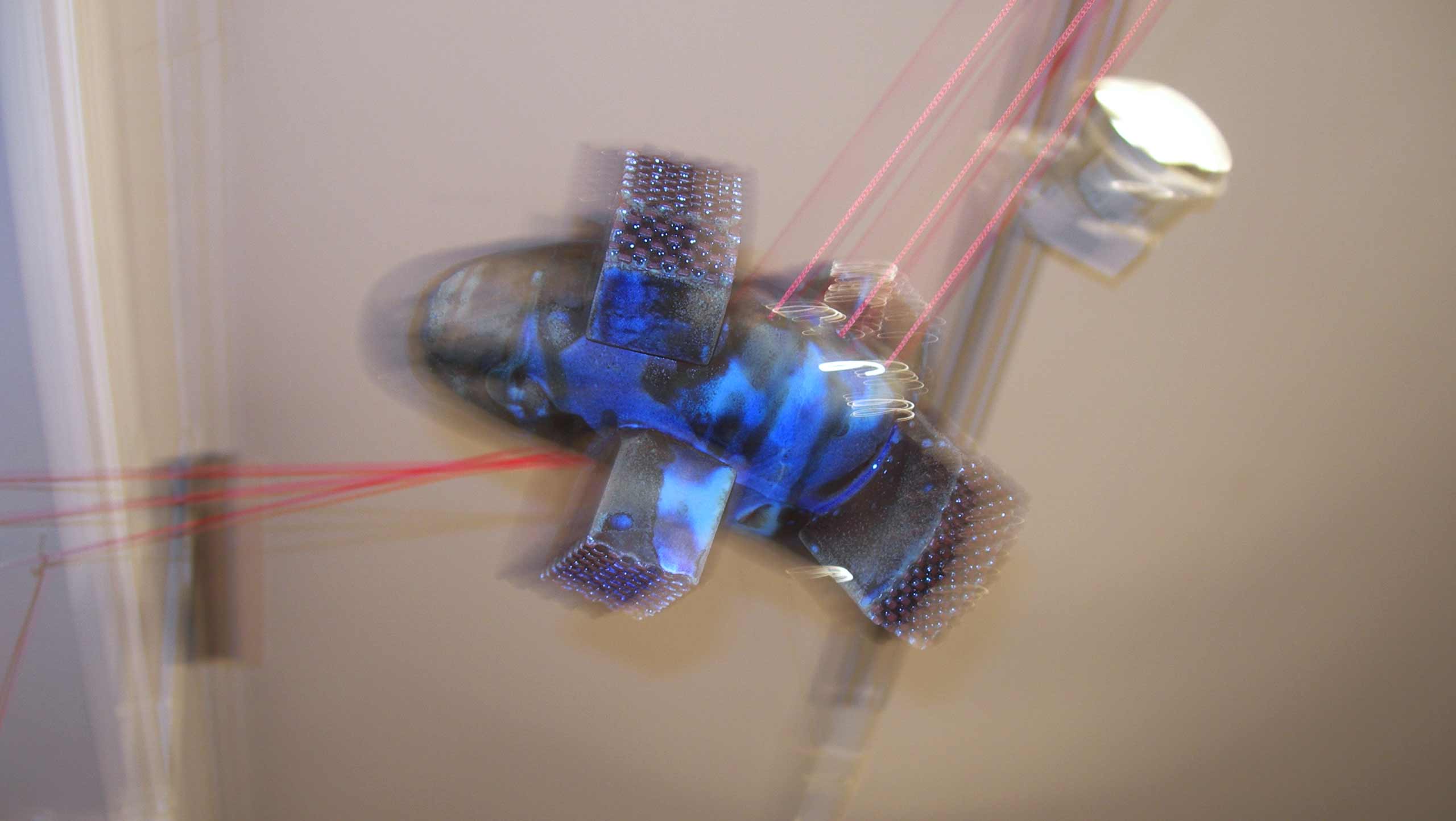 Blurred photo of 'On the threshold of destiny' a ceramic installation comprised of six ceramic objects linked together with three strands of bright red cord.