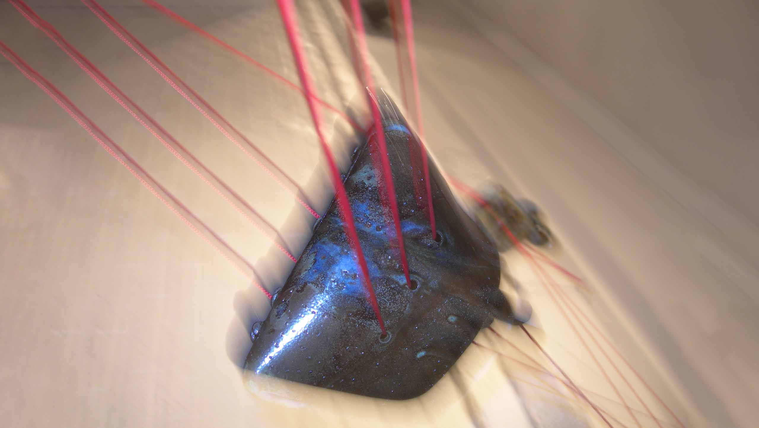 Blurred photo of one of the compositions in 'On the threshold of destiny' a ceramic installation comprised of six ceramic objects linked together with three strands of bright red cord.