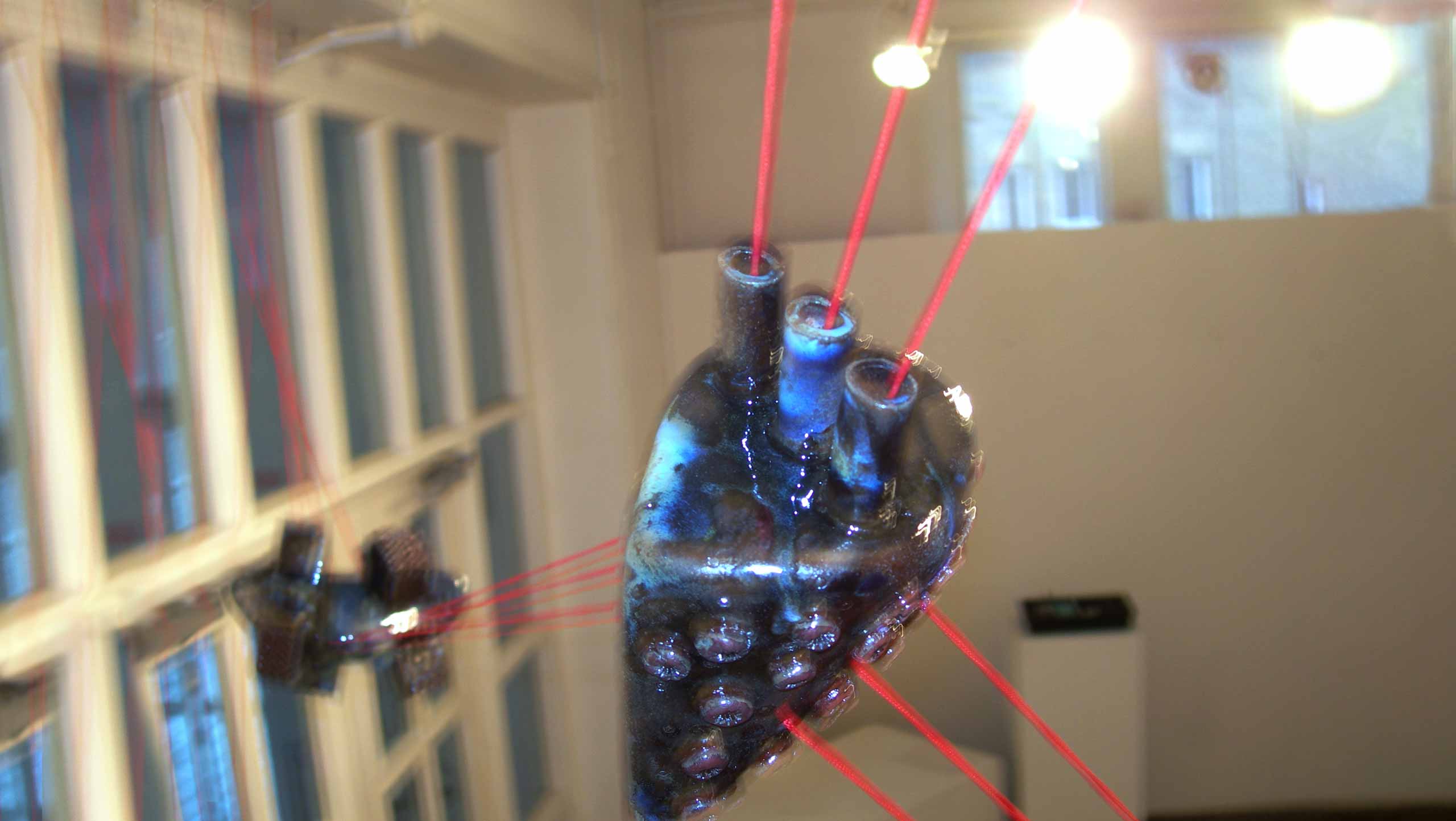 Blurred photo of one of the compositions in 'On the threshold of destiny' a ceramic installation comprised of six ceramic objects linked together with three strands of bright red cord.