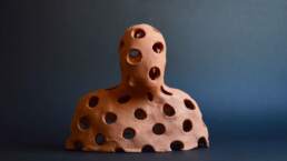 Holey Observer, A simplified head and shoulders with big even holes, from the Enlightenment installation. A single terra-cotta figure. Unglazed earthenware made by contemporary ceramic artist Simon FellEnlightenment single terra-cotta figure. Unglazed earthenware made by contemporary ceramic artist Simon Fell