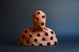 Holey Observer, A simplified head and shoulders with big even holes, from the Enlightenment installation. A single terra-cotta figure. Unglazed earthenware made by contemporary ceramic artist Simon FellEnlightenment single terra-cotta figure. Unglazed earthenware made by contemporary ceramic artist Simon Fell