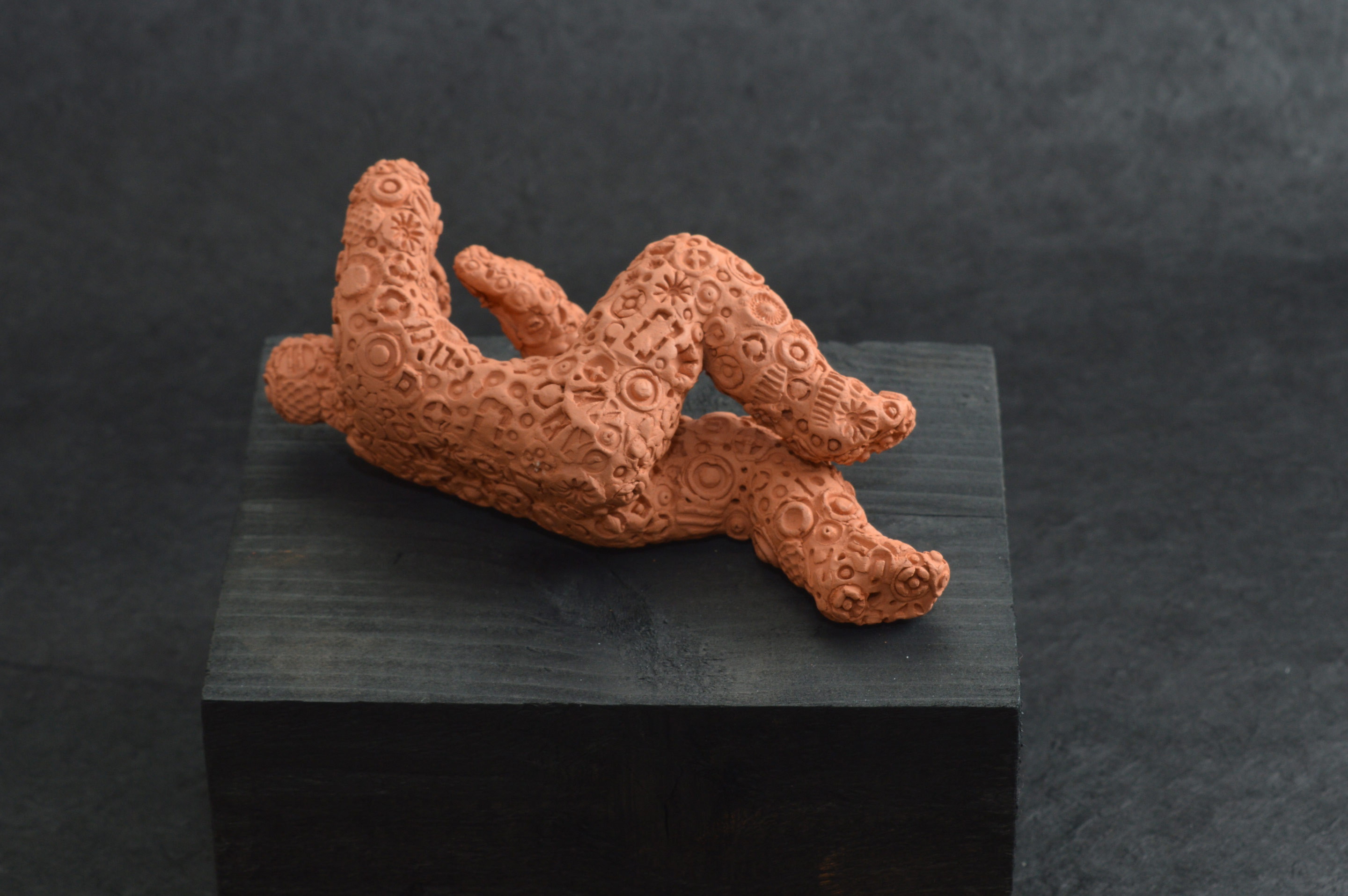Falling Figure 04, an unglazed terracotta figure about 10cm in length encrusted with embossed forms