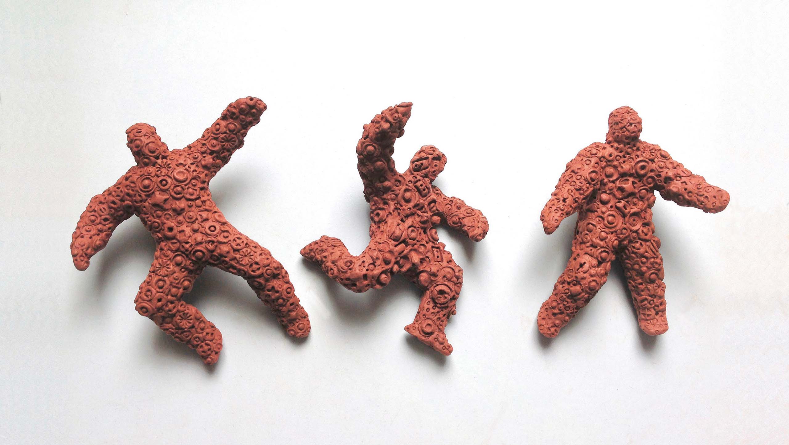 A row of three encrusted terra cotta figures on a white background