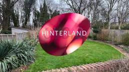 Hinterland logo variant 9 (cherry red tints) over a photograph of the Ovoid studio / project space / gallery in a garden in Ovingdean near Brighton.