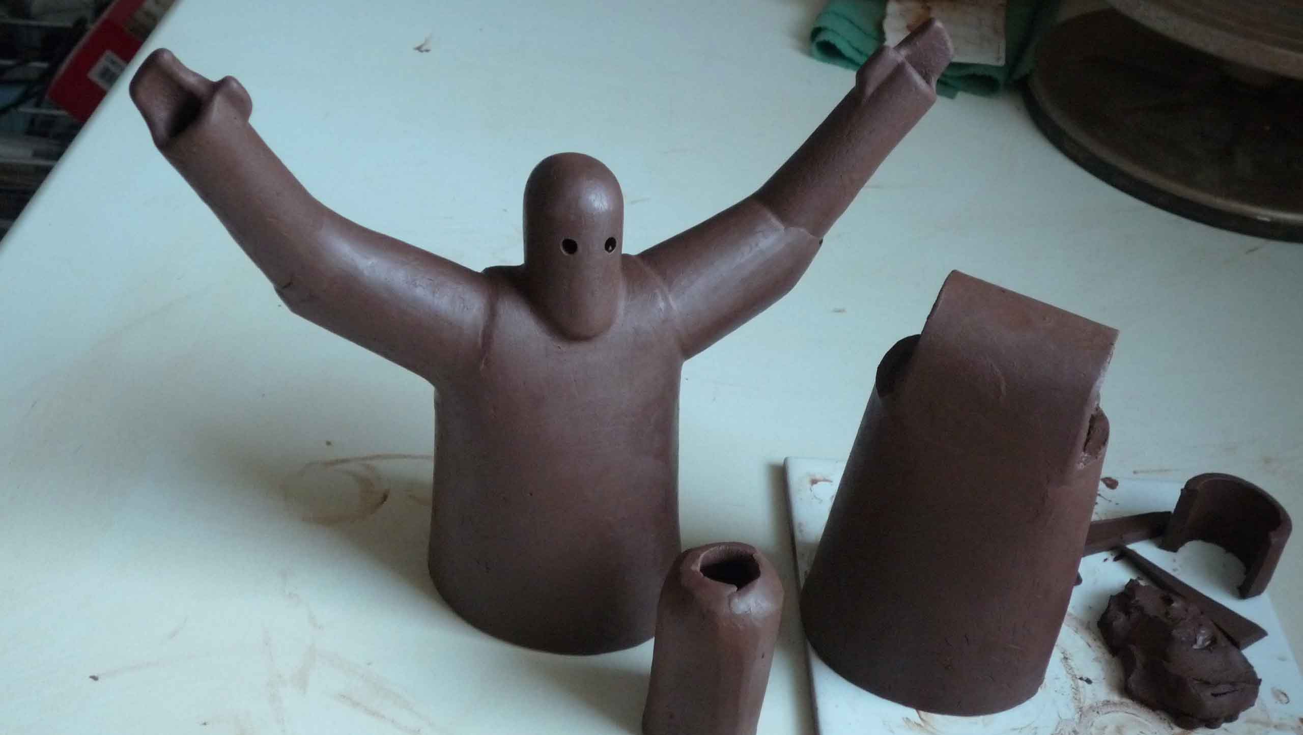 One simplified clay figure with arms raised out to the side in votive gesture. The figure is streamlined and possibly armoured with a cask-like head. Work in progress at the leather hard clay stage