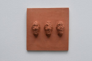 Terracotta tile with three faces in a row the faces are defaced with tiny imprinted crosses